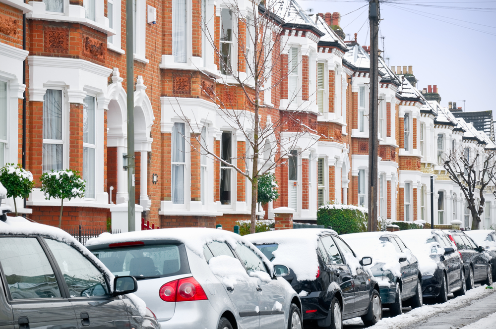 cars parked on house lined street in winter with snow